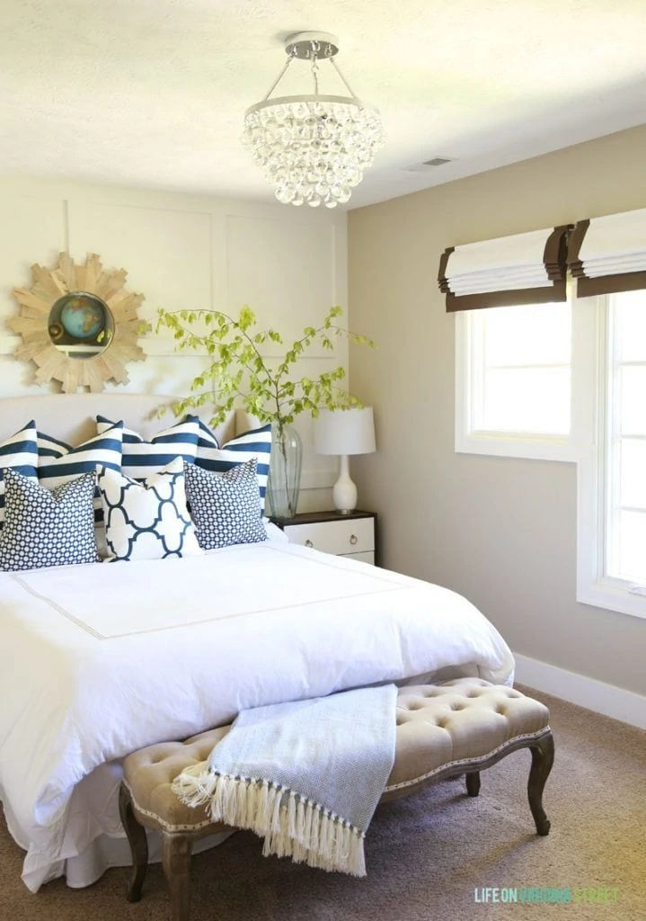 Guest bedroom with white bedding, crystal chandelier, navy striped pillows and roman shades. Love the board and batten feature wall behind the bed!