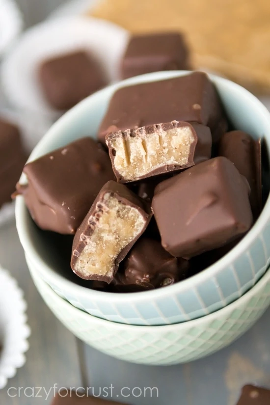Butterscotch squares that have a chocolate coating in a white bowl.