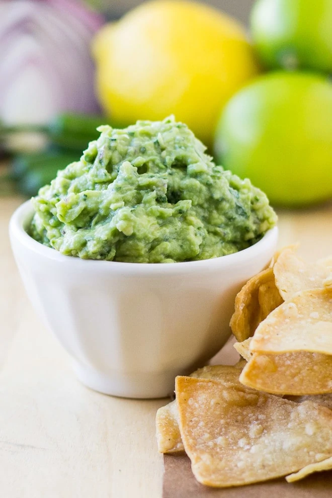 Guacamole in a white bowl on the table with corn chips beside it.