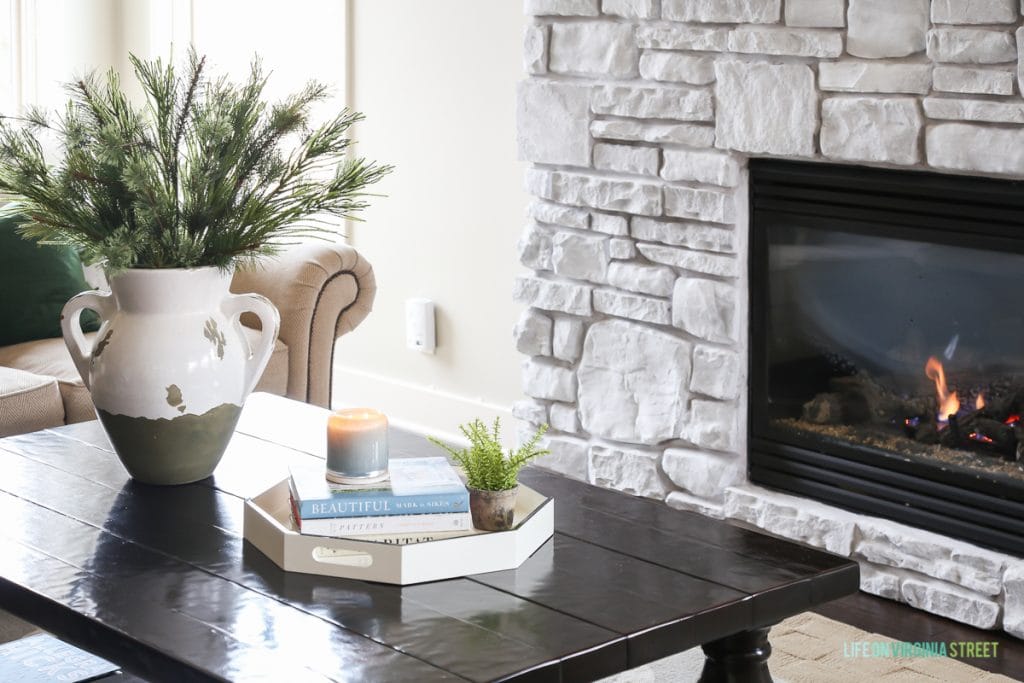 Living room coffee table with a vase, candle and book on it and a fireplace in the background.