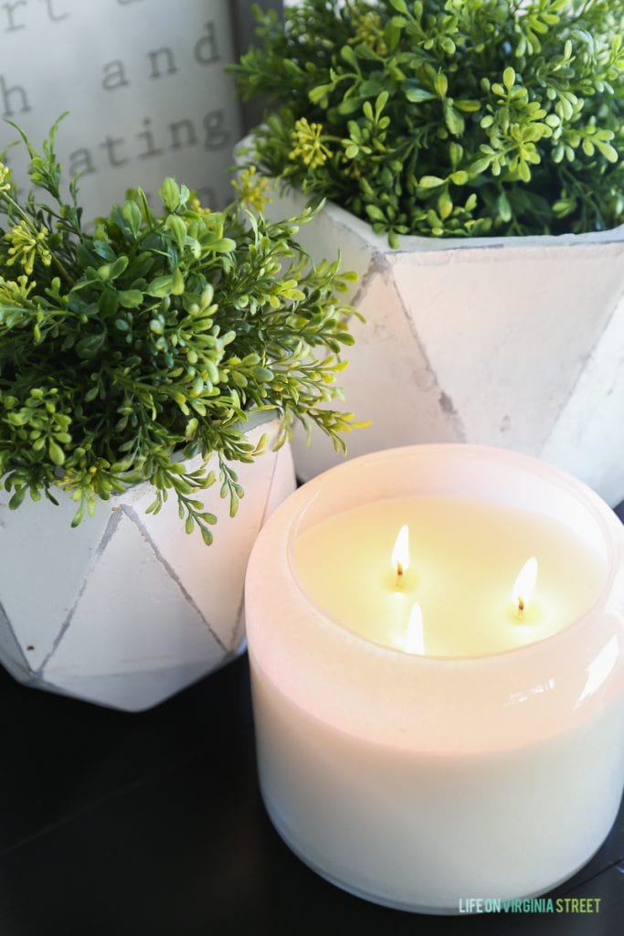 Up close picture of a candle that is lit with green plants surrounding it.