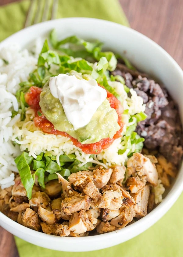 Chicken in a bowl with rice and beans and sour cream on top.