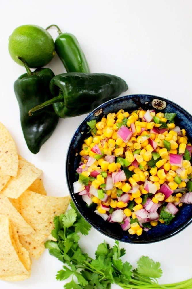 Corn salsa in a bowl with peppers beside it.