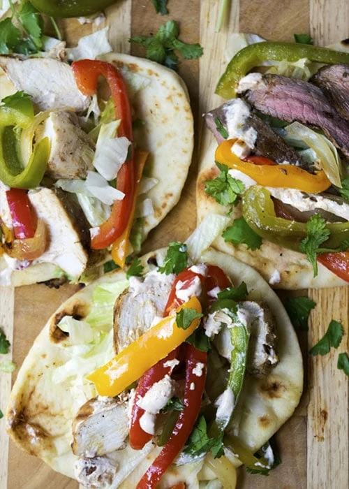 Fajita pita with green and red peppers pictured on a wooden cutting board.