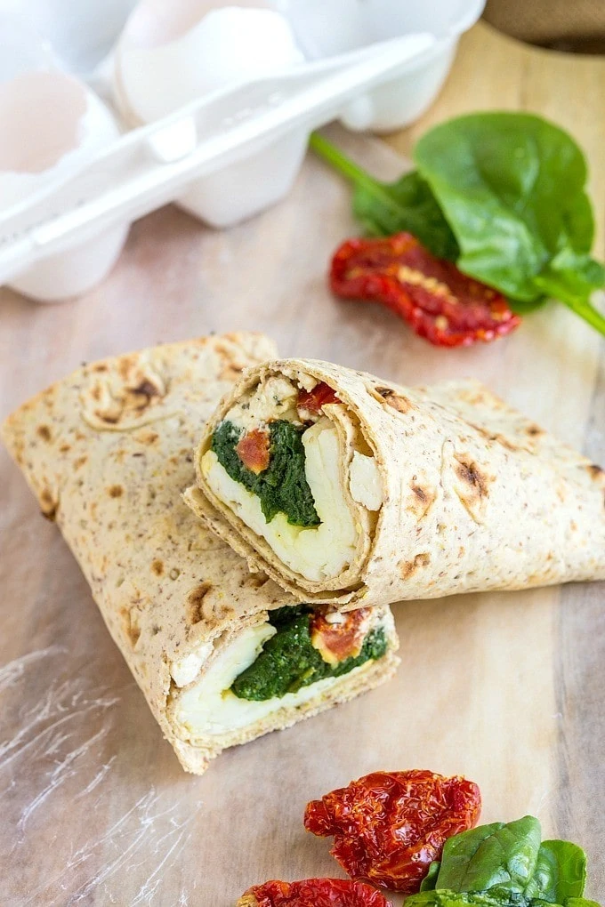 A spinach and feta breakfast wrap on the counter with spinach leaves beside it.