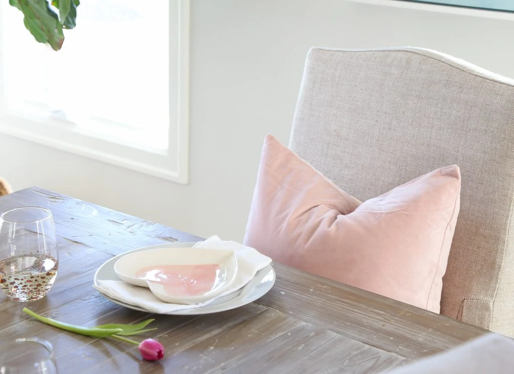 A heart shaped plate with a pink tulip beside it and a pink pillow on the chair.