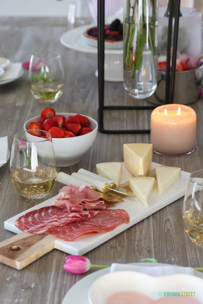 A meat and cheese tray with strawberries in a bowl and candles on the table.