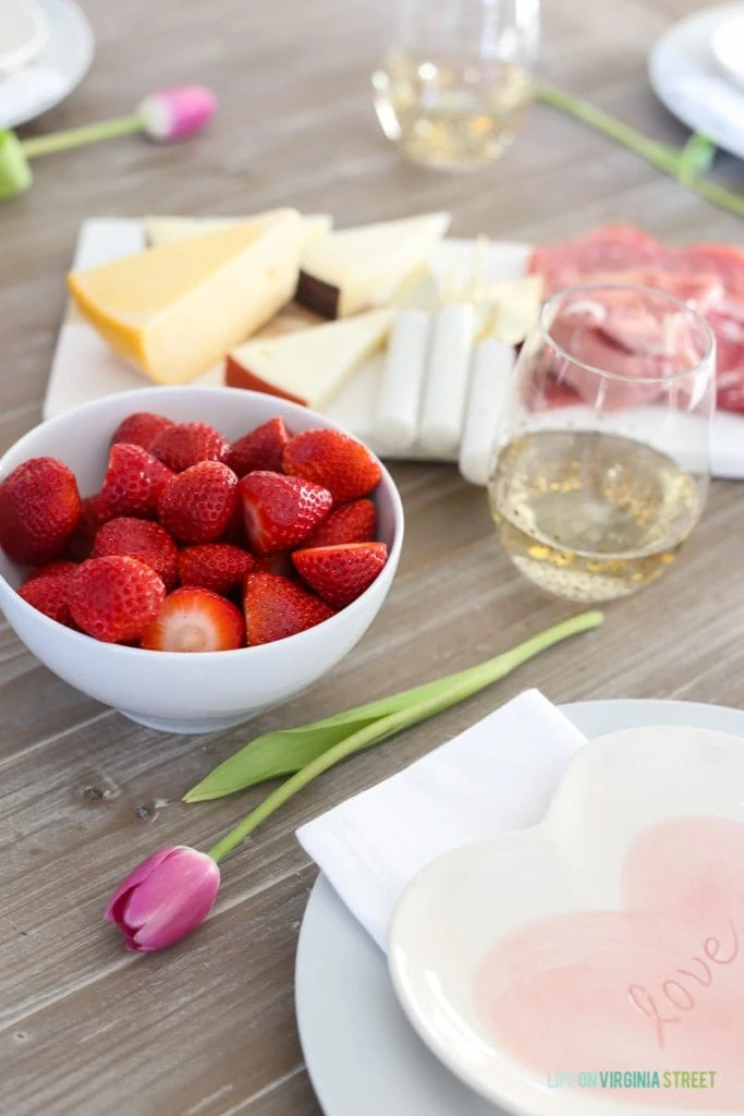 A bowl of strawberries, cheese and white wine on the table.