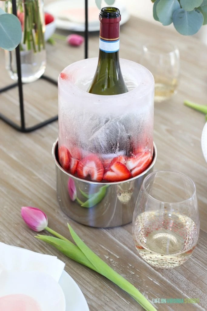 A bottle chiller with wine on the table and a tulip beside it.
