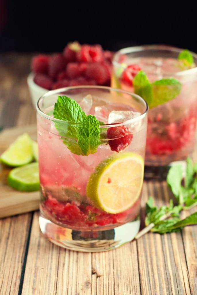 Raspberry mojitos in a clear glass with muddled raspberries and mint leaves.