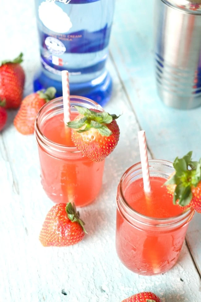 A strawberry cocktail in a mason jar with strawberries around it.