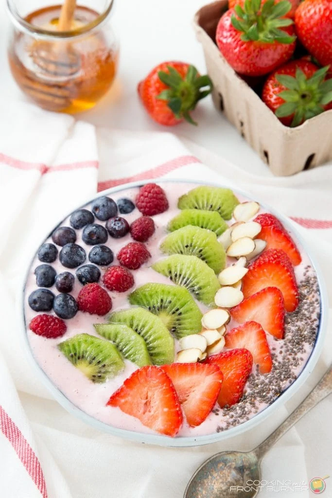 Strawberry banana smoothie bowl with honey and a container of strawberries on the counter beside it.