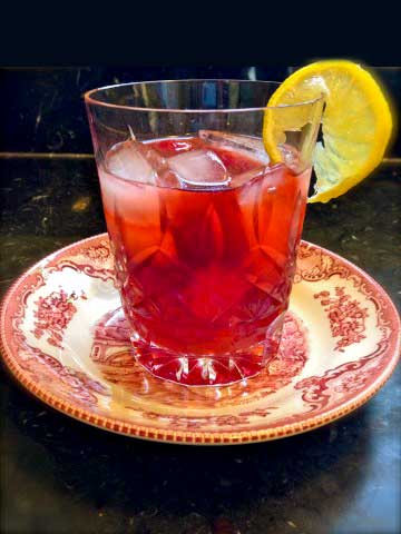 Bourbon cherry drink on a red and white plate and a lime on the side of the glass.
