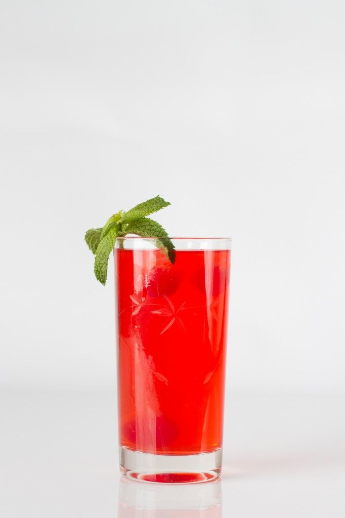 A cranberry sour in a tall glass and a mint leaf on the side of the glass.