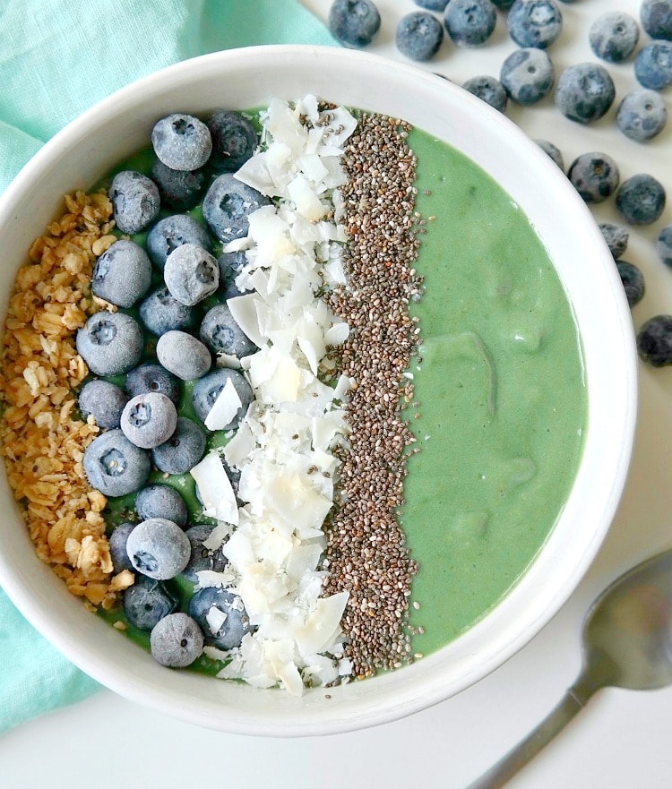 Mermaid smoothie bowl with a green base in a white bowl and blueberries on top.
