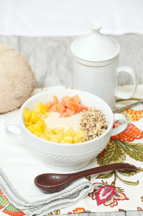 Pina colada protein smoothie bowl in a white bowl with a spoon beside it.