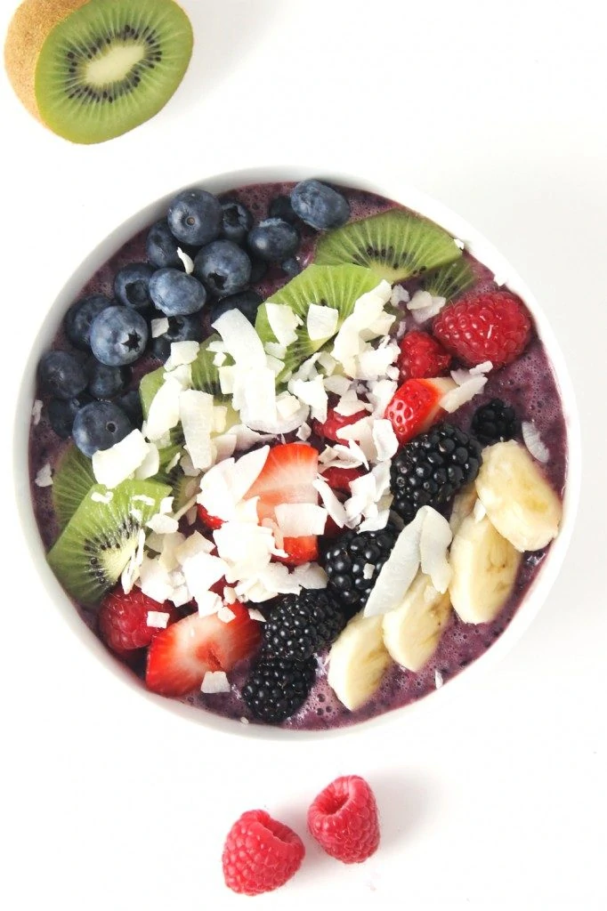 Triple berry cocnut acai bowl and two raspberries on the counter beside it and on cut kiwi fruit.