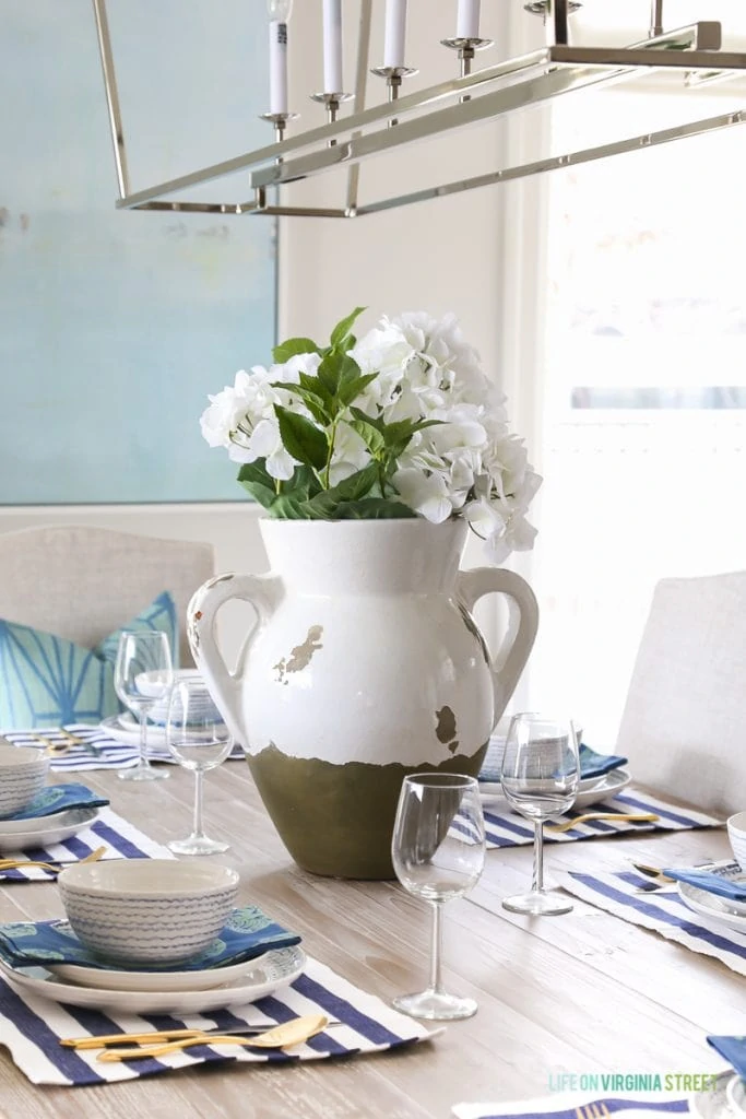 A white and olive green vase with white flowers in it on the table.