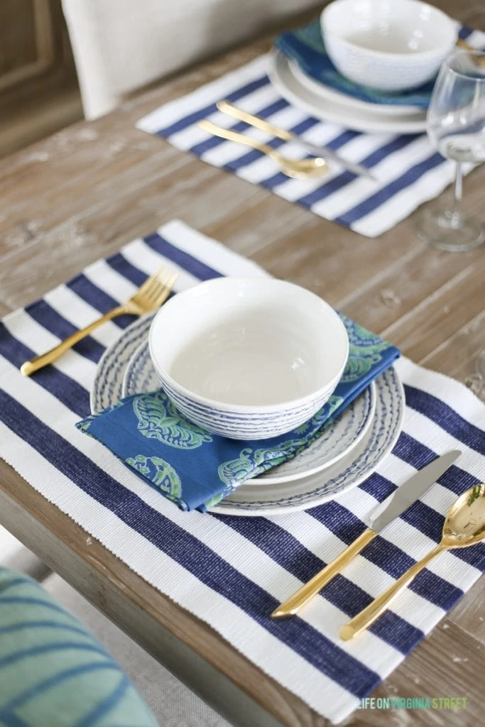 Striped placemat, a bowl, and plates and gold cutlery on the table.