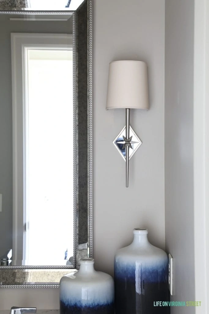 Neutral powder bathroom with Behr Castle Path walls, Benjamin Moore Hale Navy vanity cabinets, indigo ombre vases, and chrome star sconces.