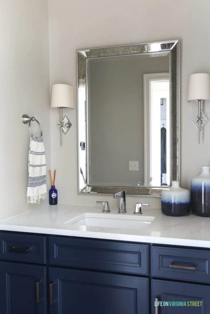 Neutral powder bathroom with Benjamin Moore Hale Navy navy blue cabinets, chrome star sconces, blue ombre vases, and Daltile One Quartz in the Luminesce.