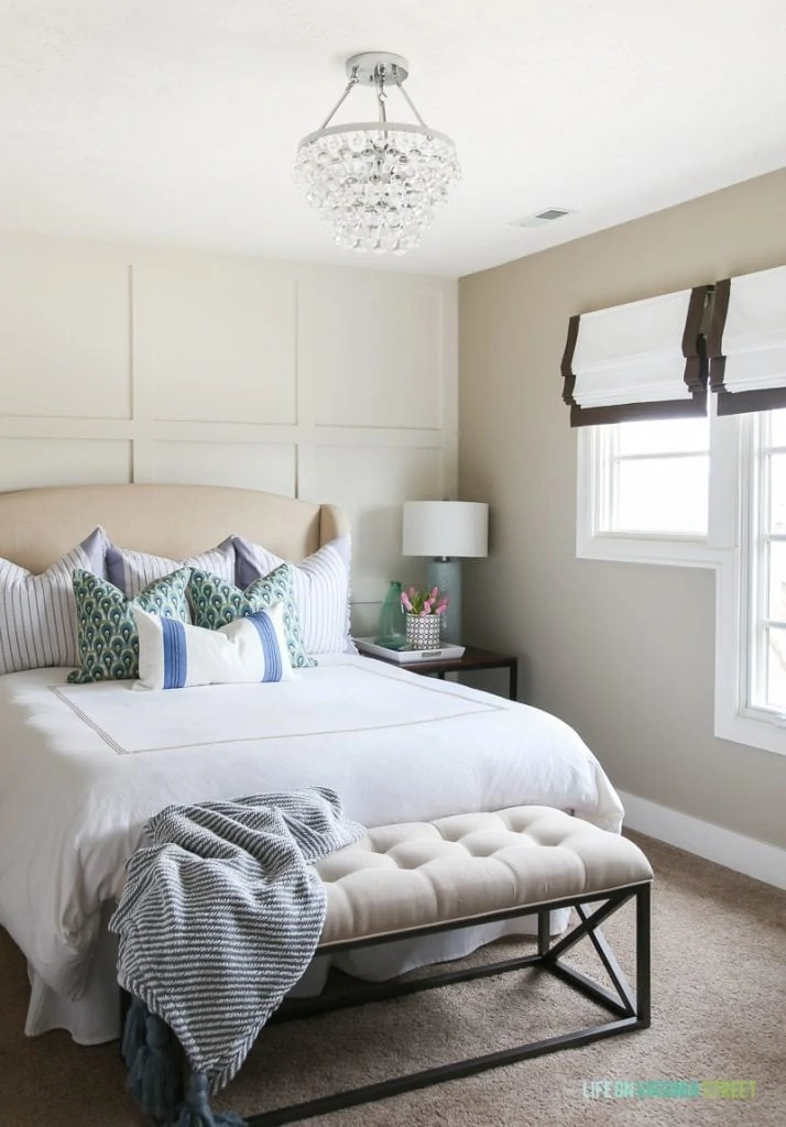Spring guest bedroom with white bedding, ribbon trimmed roman shades, glass chandelier, pink tulips, board and batten feature wall, and blue and green accents.