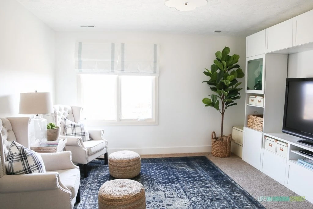 Love this craft room / TV room painted in Benjamin Moore Simply White. The IKEA BESTA stores fabric and other crafts, and the navy blue rug, fig tree and sisal poufs add color and texture. Also love that scalloped flushmount light fixture!