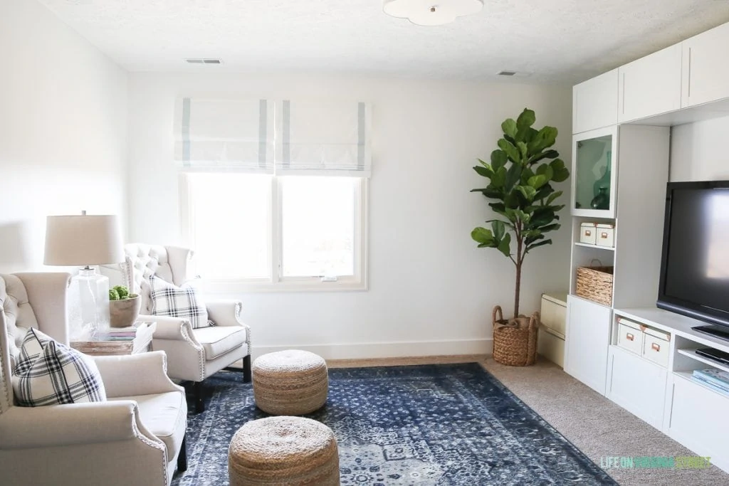 Linen chairs, blue vintage rug, ribbon trimmed roman shades, sisal poufs and Behr Simply White Walls. Love the scalloped light fixture and IKEA BESTA entertainment center!