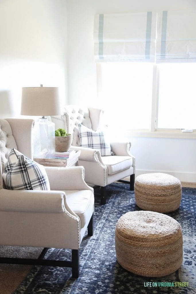 Linen chairs, blue vintage rug, ribbon trimmed roman shades, sisal poufs and Behr Simply White Walls.