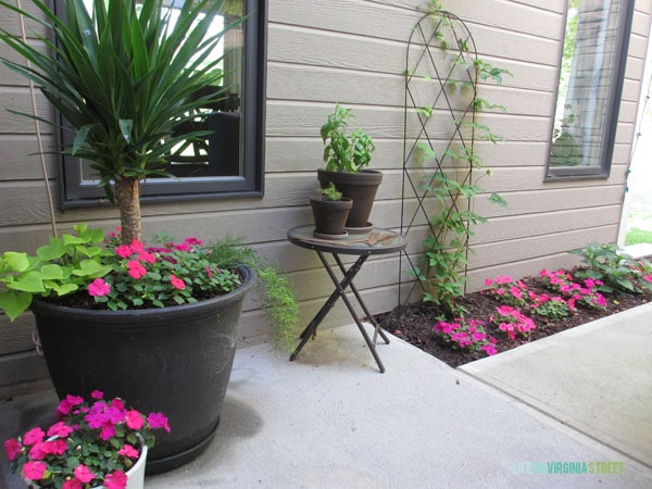 The side of the house with a small table and plants on it and large round planters.