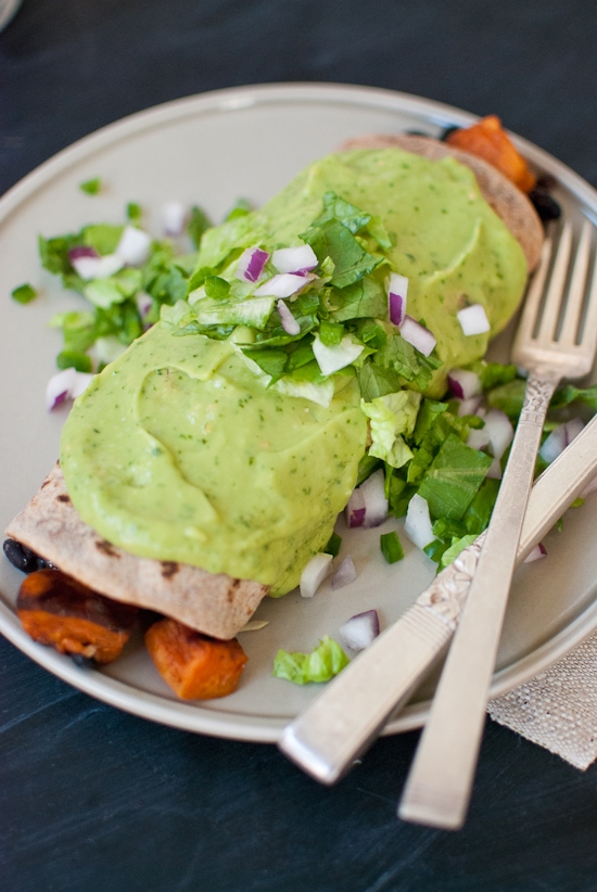 An avocado burrito on the plate with onions and lettuce on top.