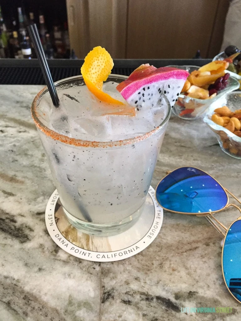 A dragan fruit mule with a black straw, orange peel and sunglasses beside the drink.