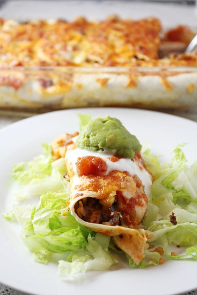 A cheesy baked burrito with a dollup of guacamole on top and shredded lettuce underneath it.