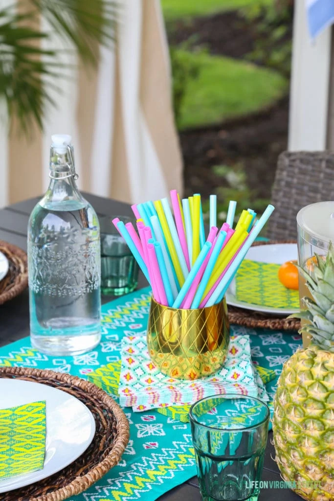 Bright pink, blue, white and yellow straws in a gold container on the table.