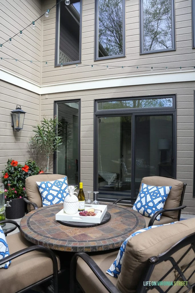 An outdoor table on the back patio with blue and white pillows on the chairs.