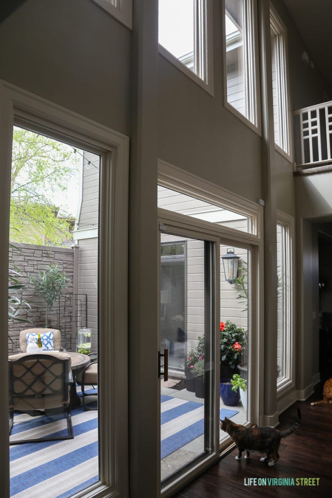 Hallway view of an outdoor courtyard entertaining space. Love the blue and white striped rug, the blue and white trellis pillows, the oleander topiaries, the limes in the beverage dispenser, the white ceramic pineapple, and more!