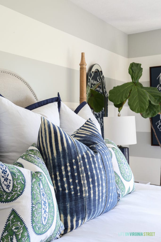 Assorted blue and green paisley pillows, against a grey and white horizontal striped wall. 