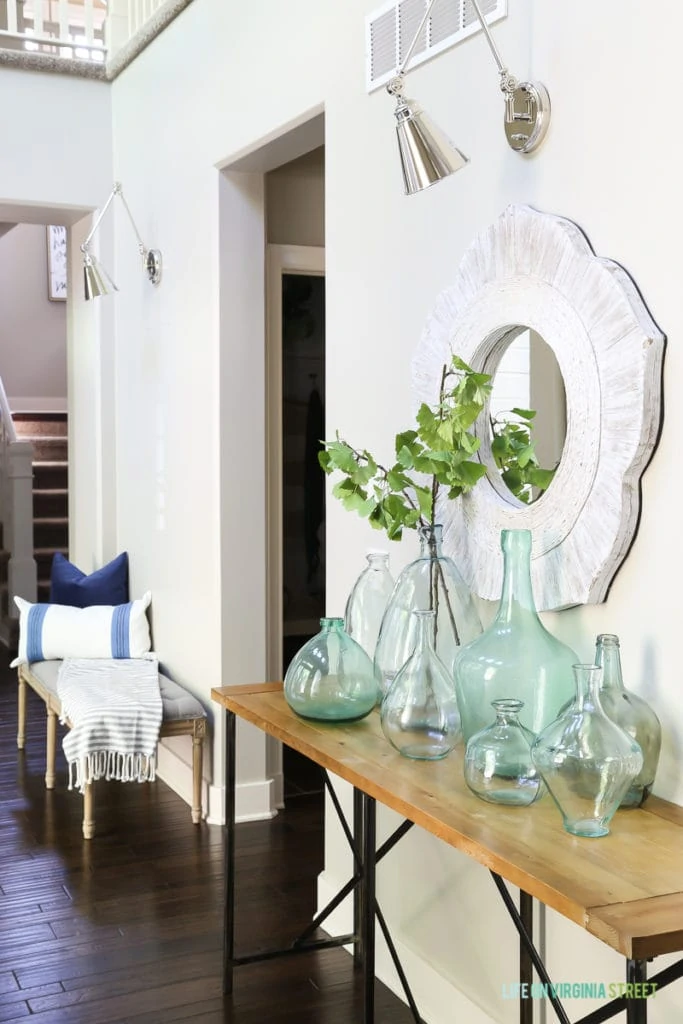 A coastal style entryway with linen bench, striped throw, blue and green recycled glass vases, polished nickel swing-arm sconces and gingko stems make the perfect beachy vibe!