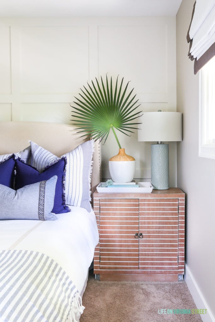 Nightstand featuring a palmetto branch, white and wood vase, aqua lamp and ribbon-trimmed roman shades. Love that striped wood!
