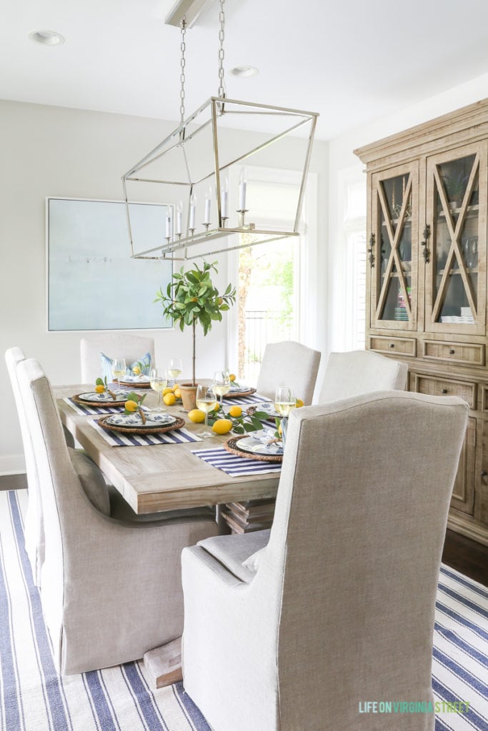 A table decorated with lemons, and a blue and white rug underneath the table. There is a Darlana light fixture above the table.