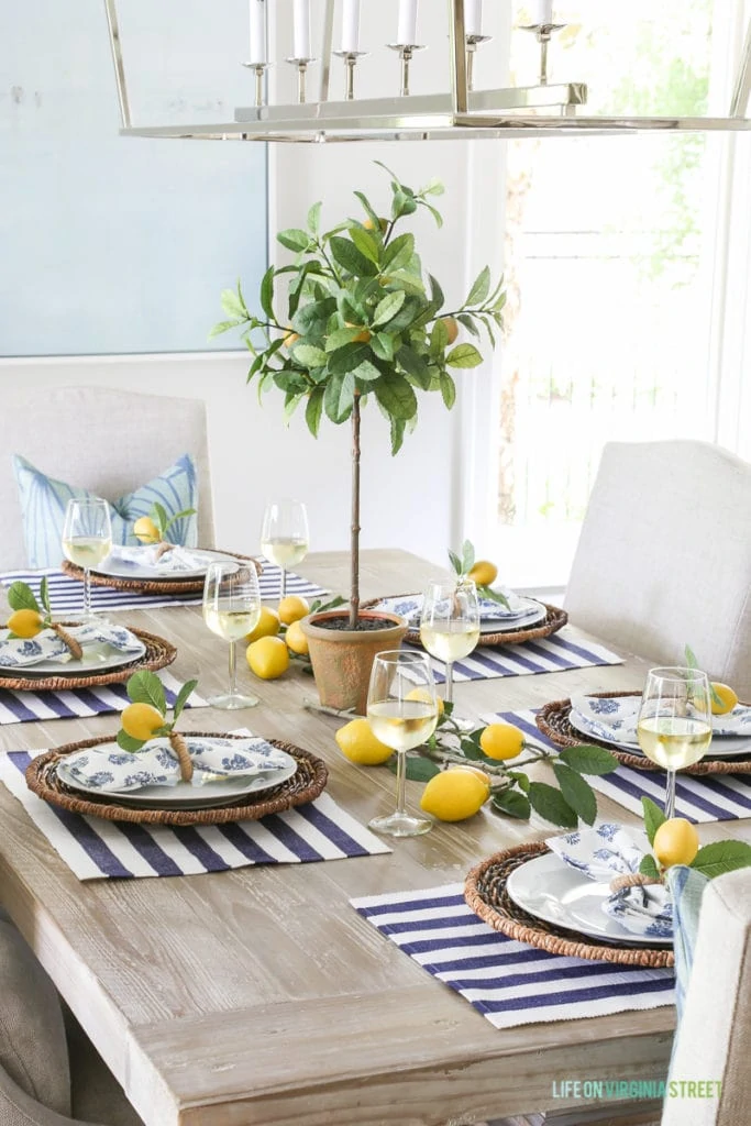 A small lemon tree in the middle of the table, with lemons on the table and also on the plate.