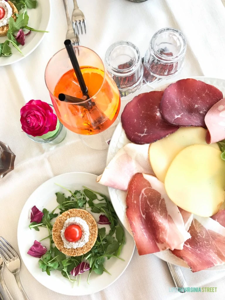 A table set with aperol spritz, salad, and meat and cheese tray.