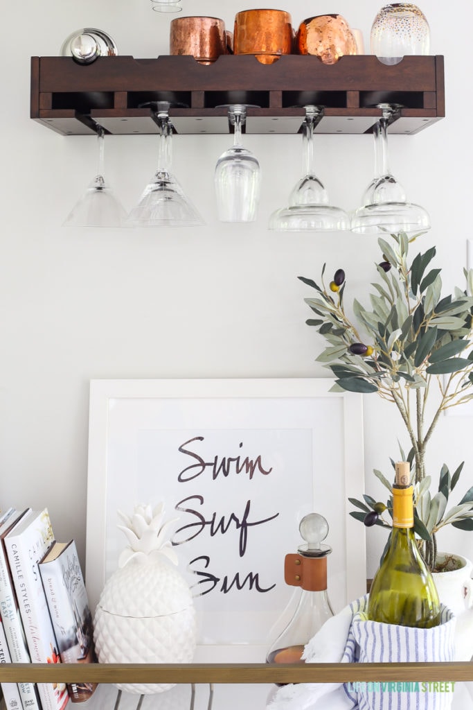 A wooden wine glass shelf with copper cups and wine glasses hanging.