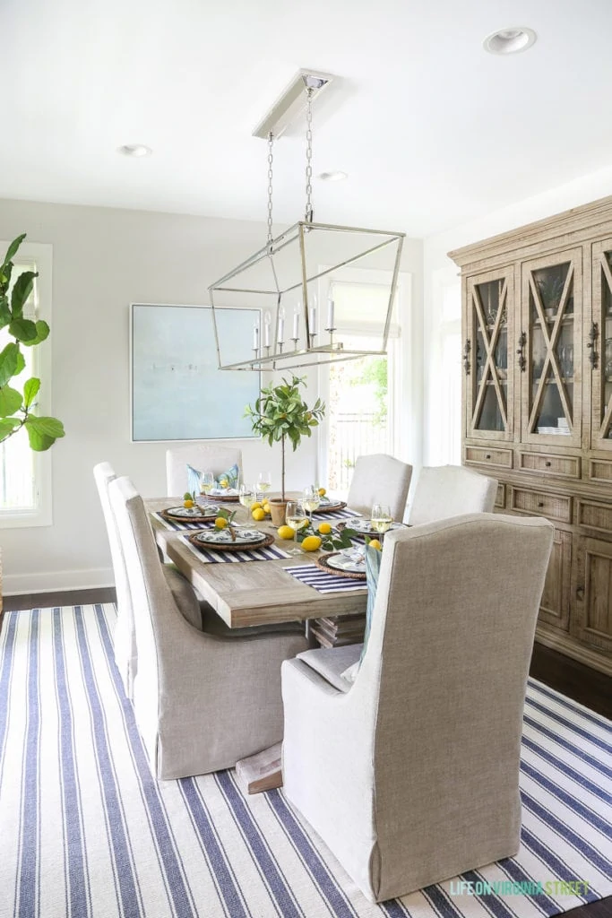 A beautiful summer tablescape inspired by the Amalfi Coast in Italy. Lemons, navy blue and white stripes, linen chairs, Darlana linear pendant, wood hutch, beach art, Dash & Albert striped rug, reclaimed wood table and wine!