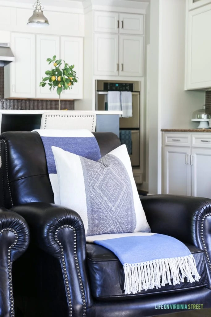 Love this idea: lighten dark leather furniture (chairs or couches) by adding a light, colorful throw over the back. This blue and white striped throw adds a coastal vibe and helps lighten the dark leather chair.