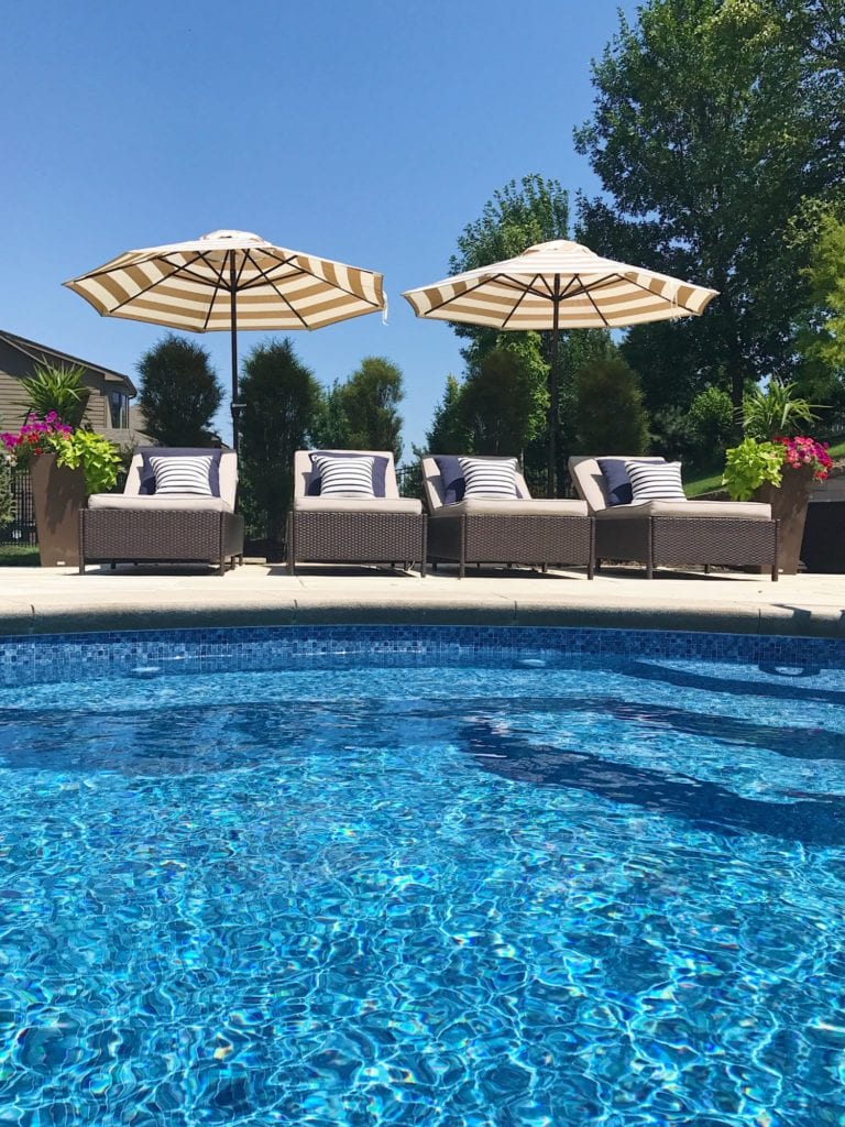 Blue vinyl pool with navy blue striped pillows on lounge chairs and beige and white striped umbrellas.