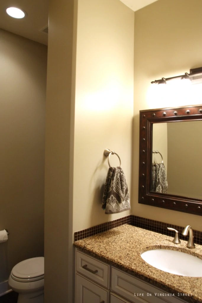 An off white bathroom with a brown mirror and speckled brown countertop.