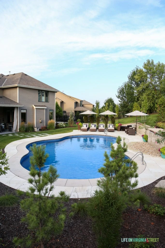 Gorgeous oasis shaped vinyl pool. Striped umbrellas, striped outdoor curtains, lounge chairs, waterfall, stone veneer, oleander and pine trees.