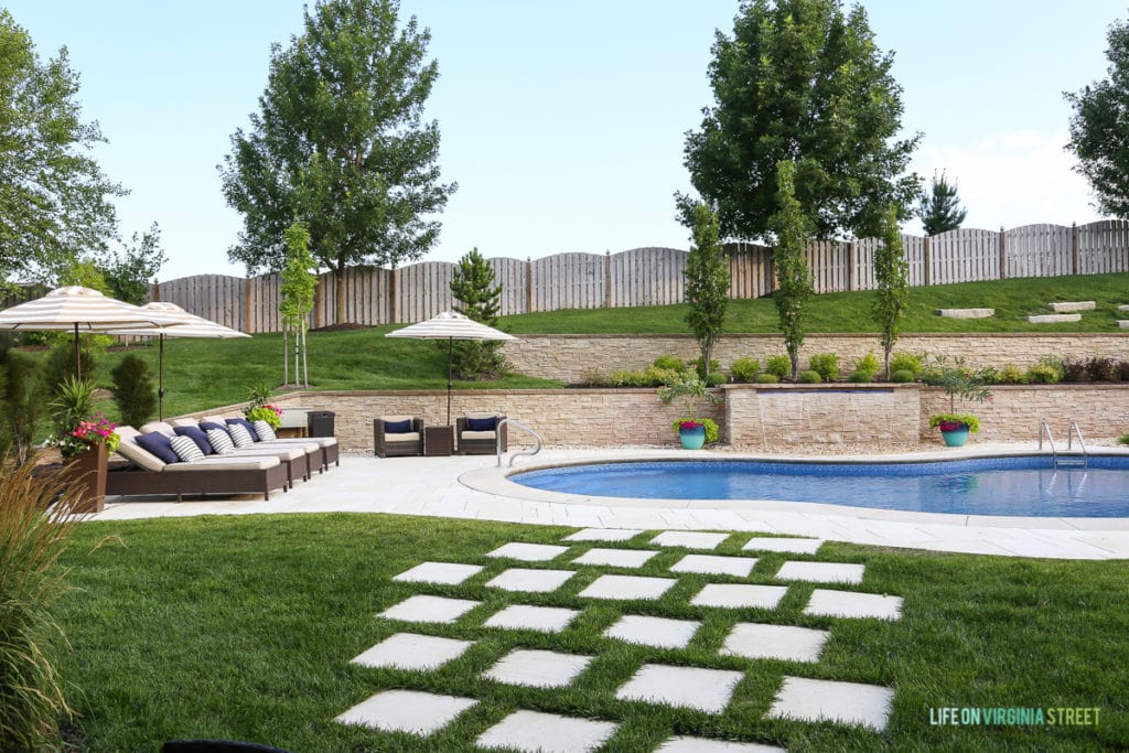 Our backyard today, with an inground pool, a deck with chairs and stepping stones in the grass.