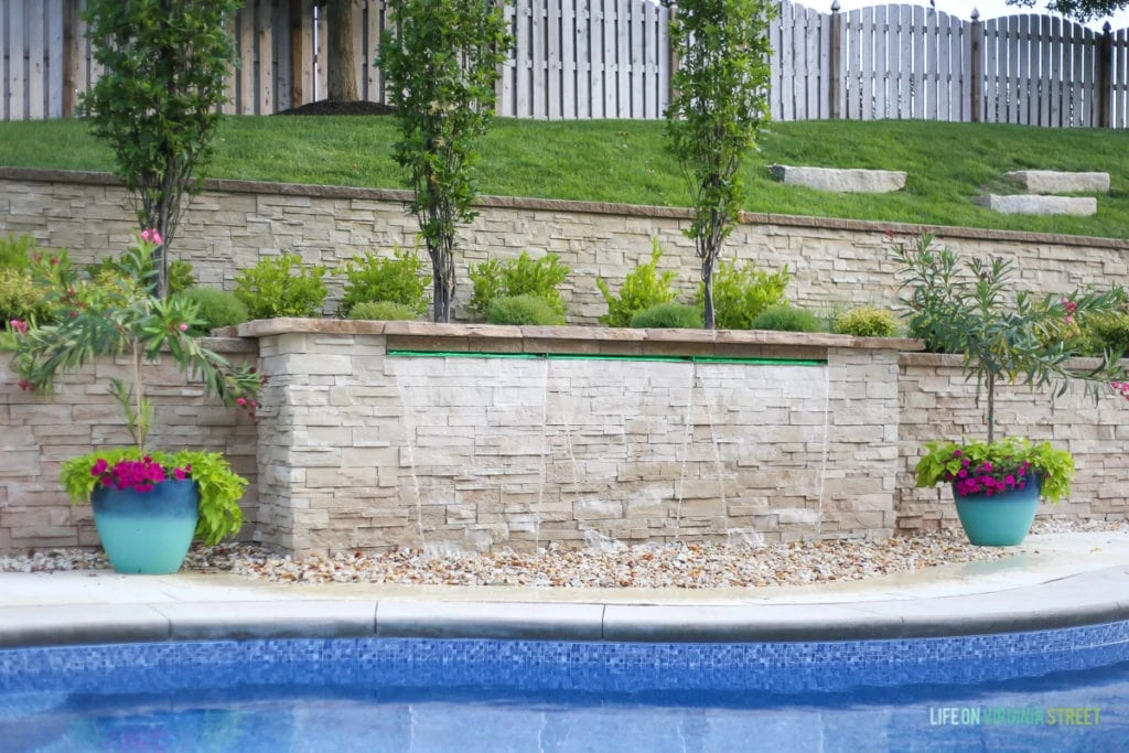 The pool waterfall feature with planters on either side of it. The pool waterfall feature with planters on either side of it. Planters are filled with oleander, sweet potato vines, and bright pink petunias.
